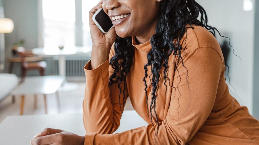 A woman smiling while having a supportive phone conversation in a bright, modern living room.